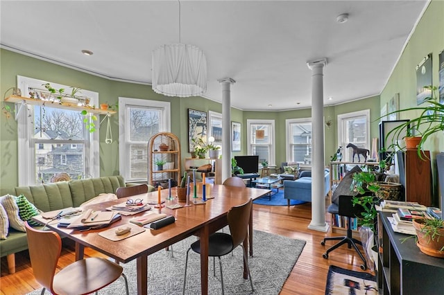 dining space featuring light wood-style floors, decorative columns, and crown molding