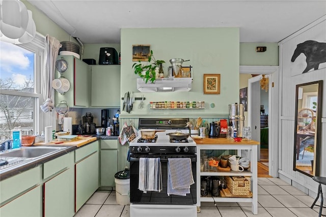 kitchen with under cabinet range hood, light tile patterned floors, green cabinets, and range with gas cooktop