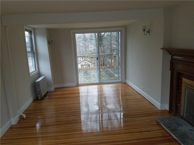 unfurnished living room with radiator, baseboards, a tiled fireplace, and wood finished floors