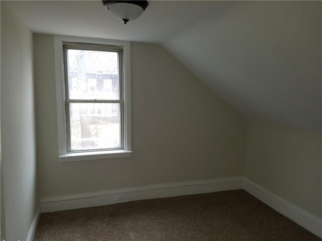 additional living space featuring vaulted ceiling, dark colored carpet, baseboards, and a healthy amount of sunlight