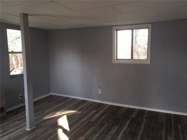 basement featuring dark wood-style floors, a drop ceiling, a wealth of natural light, and baseboards