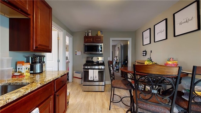 kitchen with appliances with stainless steel finishes, light wood-type flooring, light stone counters, and reddish brown cabinets