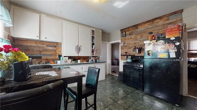 kitchen with white cabinets, wooden walls, and black appliances