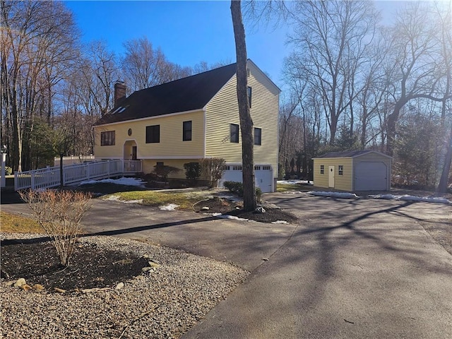 view of home's exterior with an outbuilding, aphalt driveway, a chimney, and an attached garage