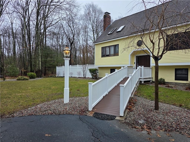 exterior space with roof with shingles, a lawn, a chimney, and fence