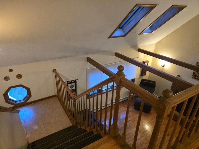 staircase featuring vaulted ceiling with skylight, a baseboard radiator, tile patterned floors, and baseboards