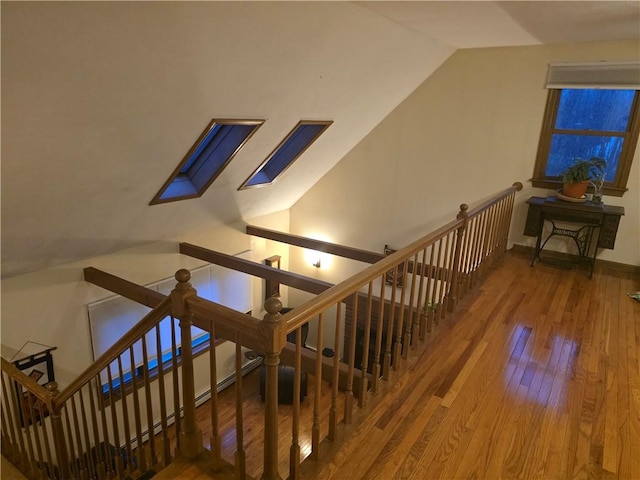 staircase with hardwood / wood-style flooring, vaulted ceiling with skylight, and baseboards