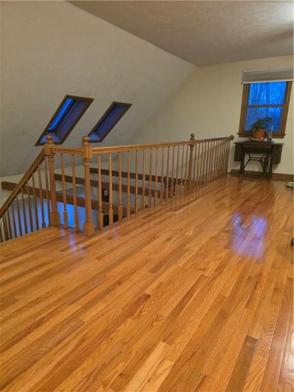 additional living space featuring vaulted ceiling with skylight and wood finished floors