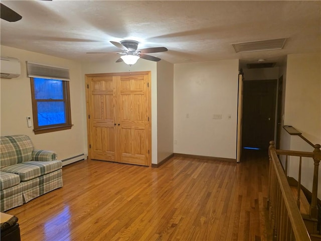 unfurnished living room with baseboards, visible vents, wood finished floors, baseboard heating, and a wall mounted AC