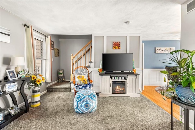 living area featuring visible vents, a glass covered fireplace, wood finished floors, stairs, and a decorative wall