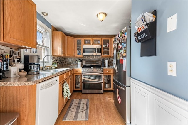 kitchen with stainless steel appliances, brown cabinetry, a sink, and wood finished floors