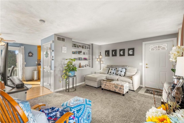 living area featuring a ceiling fan, visible vents, a textured ceiling, and wainscoting