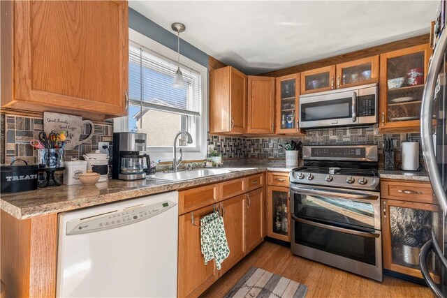 kitchen featuring stainless steel appliances, light wood finished floors, a sink, and brown cabinets