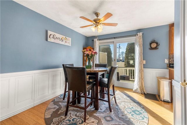 dining area featuring visible vents, a wainscoted wall, ceiling fan, and light wood-style flooring