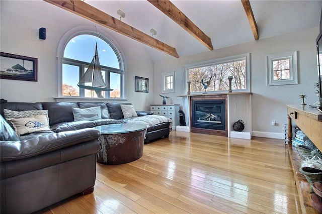 living area featuring high vaulted ceiling, baseboards, light wood-style floors, beamed ceiling, and a glass covered fireplace