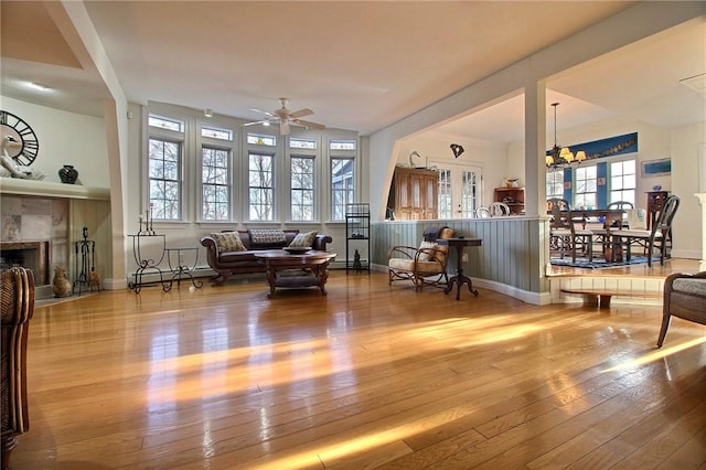 living room with ceiling fan with notable chandelier, baseboard heating, wood-type flooring, and a tile fireplace