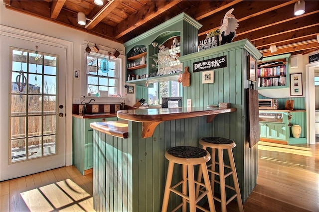 bar with wooden ceiling, light wood-style floors, bar area, and beamed ceiling