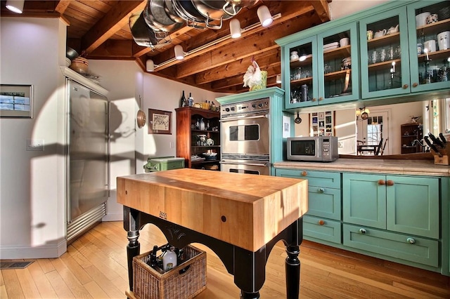 kitchen featuring wooden counters, appliances with stainless steel finishes, light wood finished floors, beamed ceiling, and green cabinetry