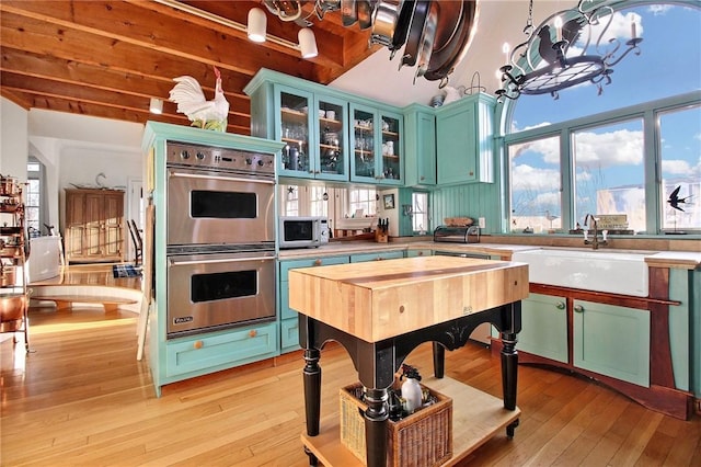 kitchen featuring light wood-style flooring, a sink, appliances with stainless steel finishes, glass insert cabinets, and an inviting chandelier