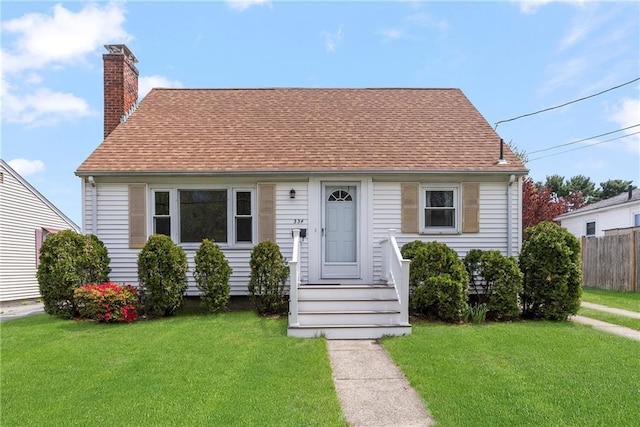 view of front of home with roof with shingles, fence, a chimney, and a front lawn