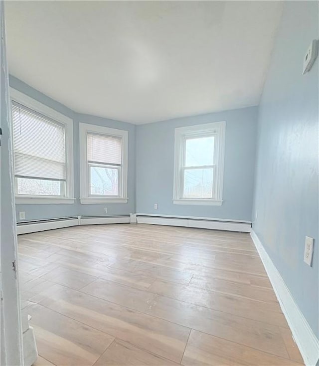 empty room featuring a healthy amount of sunlight, light wood finished floors, a baseboard radiator, and baseboards