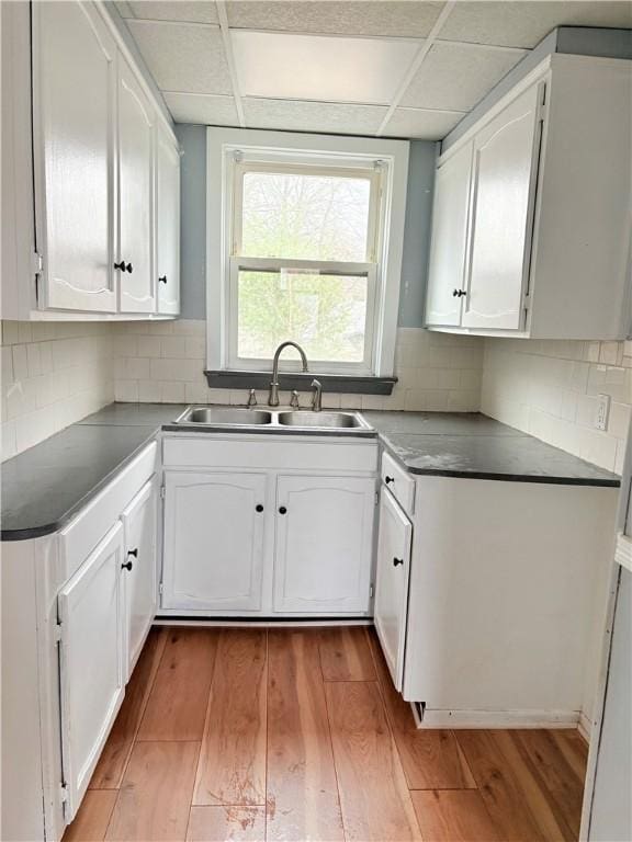 kitchen with tasteful backsplash, a sink, light wood-style flooring, and white cabinetry