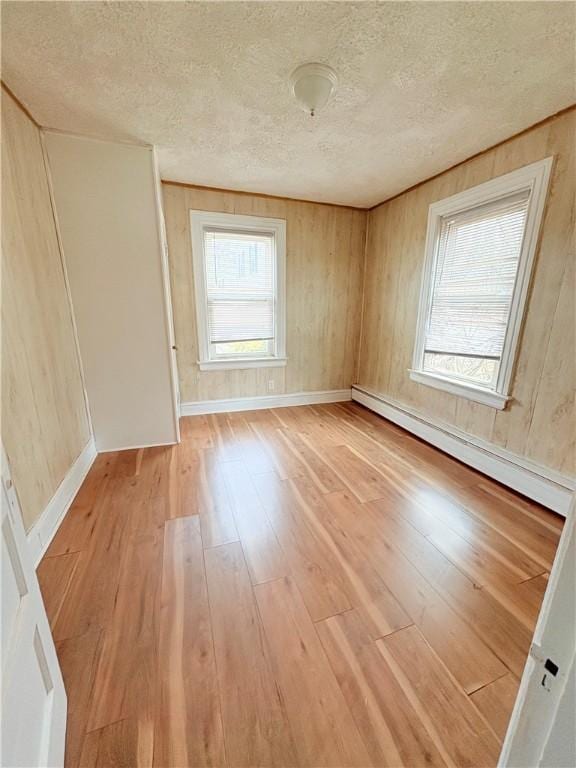 spare room featuring a baseboard heating unit, plenty of natural light, a textured ceiling, and light wood finished floors