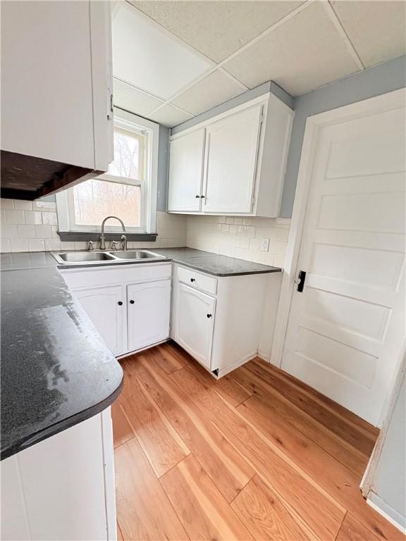 kitchen featuring light wood-type flooring, decorative backsplash, white cabinets, and a sink