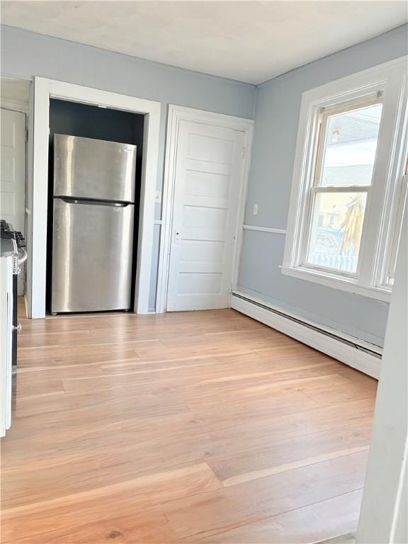 interior space featuring light wood finished floors, a baseboard heating unit, and freestanding refrigerator