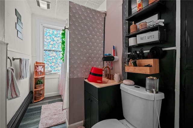 bathroom with a textured ceiling, toilet, wood finished floors, visible vents, and a sink