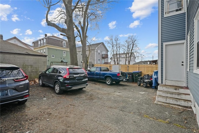 view of parking / parking lot with entry steps, fence, and a residential view