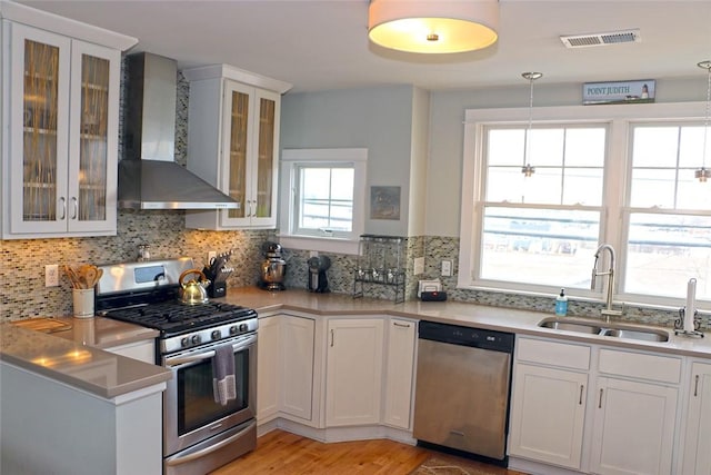 kitchen with light countertops, appliances with stainless steel finishes, white cabinets, a sink, and wall chimney exhaust hood