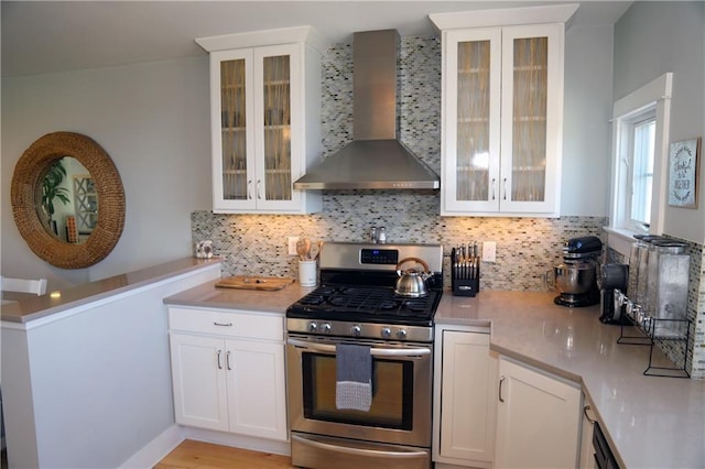 kitchen with wall chimney exhaust hood, stainless steel gas range, decorative backsplash, and white cabinets