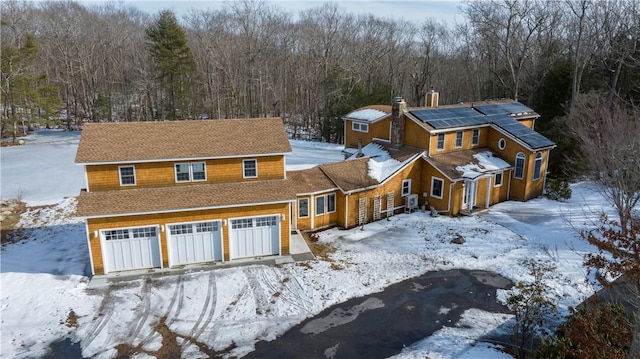 view of front facade featuring a view of trees, an attached garage, and roof mounted solar panels