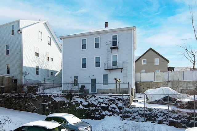 snow covered rear of property with a chimney and fence