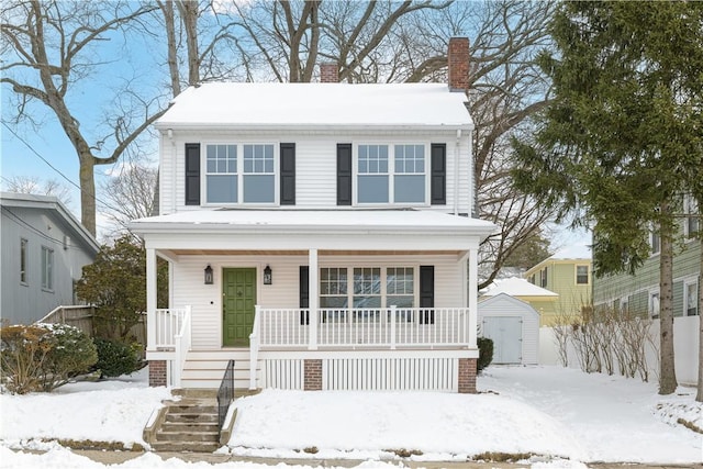 traditional style home featuring a porch, an outdoor structure, fence, a storage unit, and a chimney