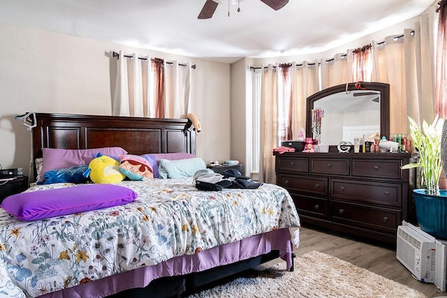 bedroom featuring a wall mounted AC, light wood-style flooring, and a ceiling fan