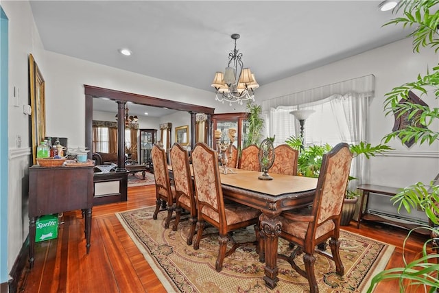 dining space with a chandelier, plenty of natural light, wood finished floors, and decorative columns