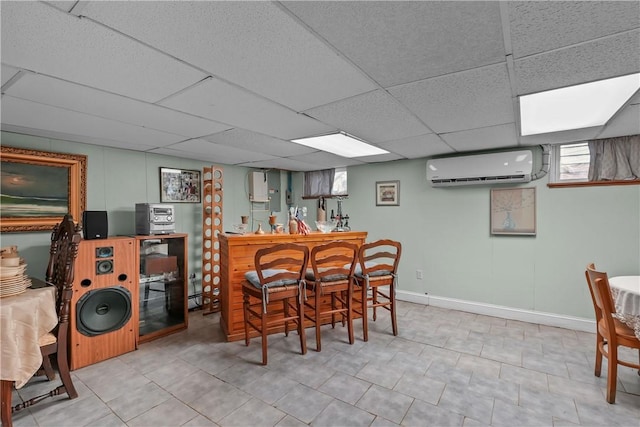 dining space featuring baseboards, a paneled ceiling, a wall unit AC, tile patterned flooring, and a bar