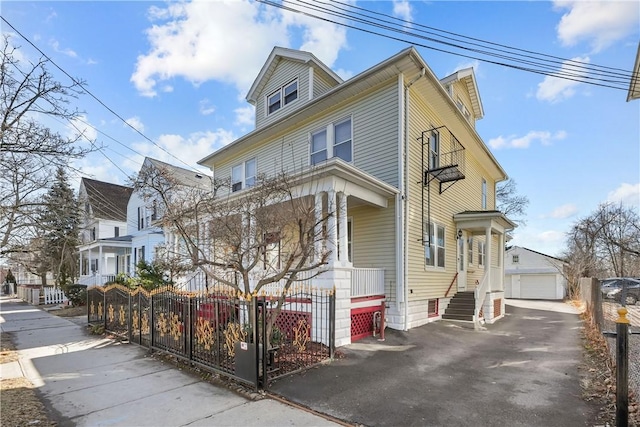 american foursquare style home with entry steps, aphalt driveway, a fenced front yard, a garage, and an outdoor structure