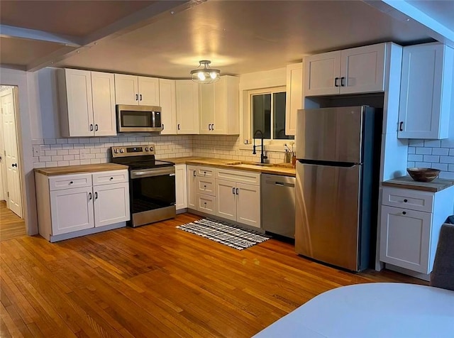 kitchen with tasteful backsplash, hardwood / wood-style floors, appliances with stainless steel finishes, white cabinets, and a sink