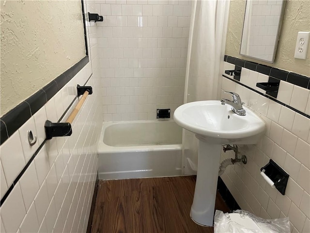 bathroom with shower / tub combo, wainscoting, a textured wall, wood finished floors, and tile walls