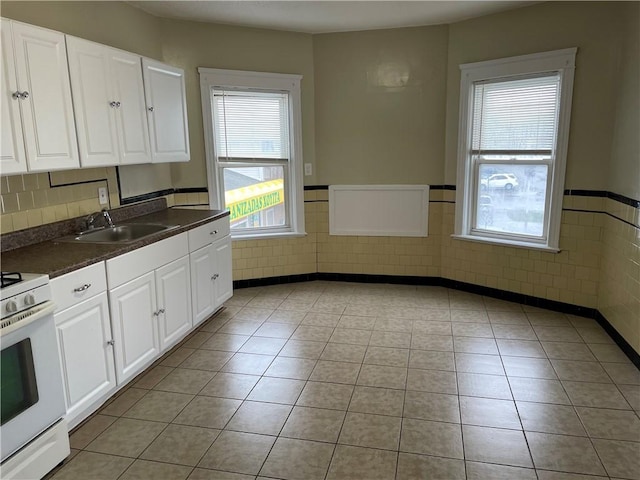 kitchen with dark countertops, a healthy amount of sunlight, light tile patterned flooring, a sink, and white gas range oven