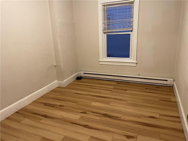 spare room with baseboards, a baseboard heating unit, and wood finished floors