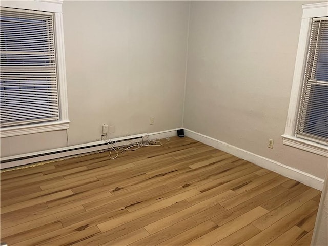 empty room with a baseboard heating unit, baseboards, and light wood finished floors