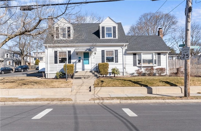 cape cod-style house with a shingled roof, fence, and a front lawn