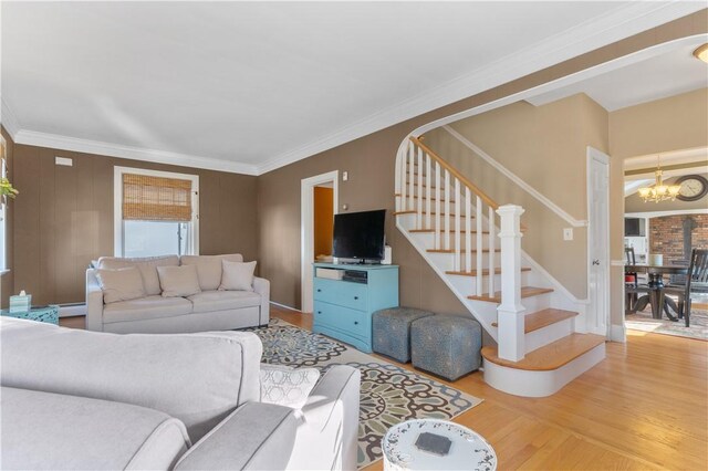 living area featuring a notable chandelier, stairway, ornamental molding, a baseboard heating unit, and wood finished floors