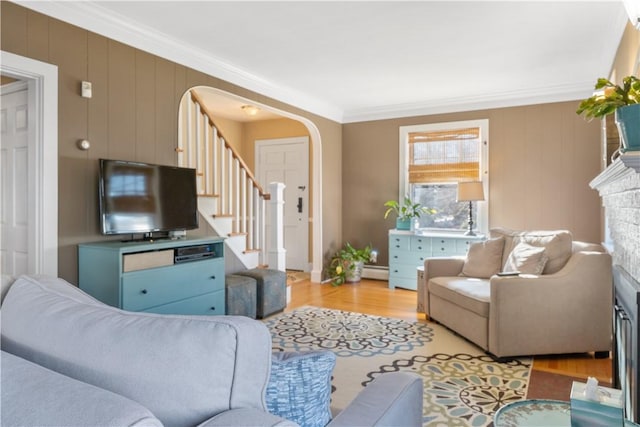 living room with arched walkways, a fireplace, stairs, ornamental molding, and light wood finished floors