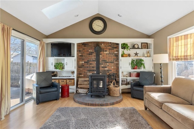 living room with a wood stove, light wood-type flooring, and vaulted ceiling with skylight