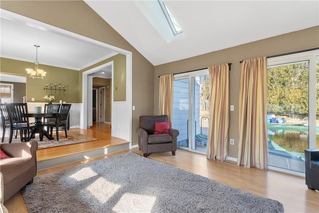 living area featuring a notable chandelier, crown molding, lofted ceiling with skylight, wainscoting, and wood finished floors